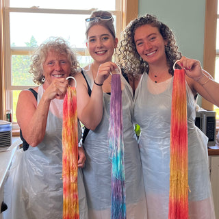 three women in aprons showing off their dyed skeins of yarn